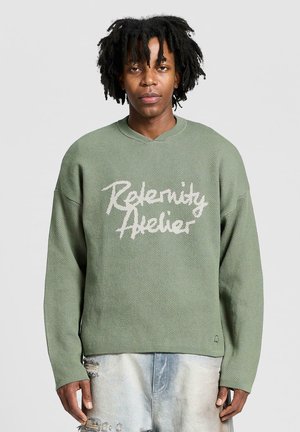 Jasnozielony, oversize sweter z teksturowanej tkaniny, z dekoltem w serek i białym nadrukiem tekstu "Relenity Atelier" na przodzie.