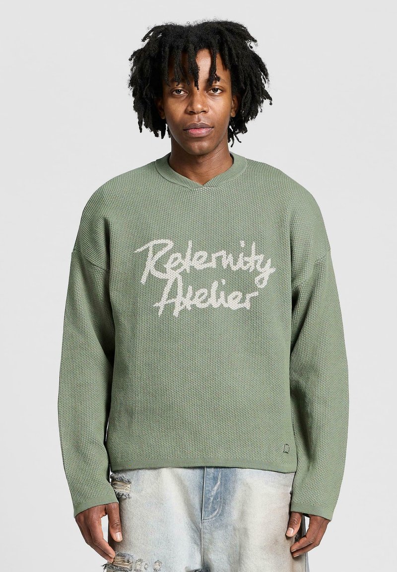 Lichtgroene oversized trui van gestructureerde stof, met een V-hals en witte bedrukte tekst "Relenity Atelier" aan de voorkant.