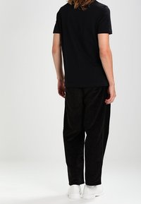 Svart kortärmad t-shirt som är ihopparad med löst sittande svarta manchesterbyxor och vita sneakers, sedd bakifrån.