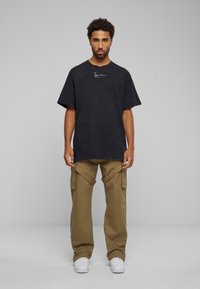Musta oversized t-särk, millel on diskreetne logo, koos khaki värvi cargo-pükstega, millel on küljetaskud. Valged tossud täiendavad väljanägemist.