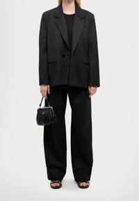 Czarna, oversize'owa marynarka wykonana z teksturowanej tkaniny, zestawiona z luźnymi czarnymi spodniami, czarnym topem i małą czarną torebką. Stylizację dopełniają płaskie sandały.