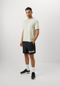 Fényes zöld, kerek nyakú, rövid ujjú póló, fekete rövidnadrággal párosítva, melyen fehér "NIKE" logó található. A modellen fekete sportcipő és fehér zokni van.
