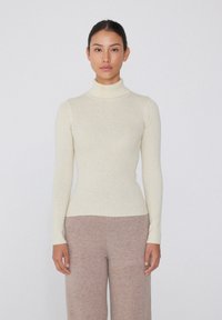 Rippstrick-Turtleneck-Pullover in cremigem Weiß, taillierte Passform mit langen Ärmeln, kombiniert mit hellbraunen weiten Hosen. Weiche Textur, minimalistische Gestaltung.