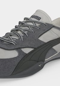 Сив и бял маратонка Puma с текстурирани връзки, алени от велур и черно лого Puma отстрани и на подметката.