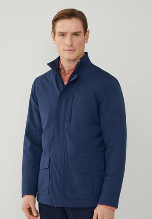 Chaqueta azul marino con cuello alto, bolsillo en el pecho con cremallera y dos bolsillos frontales. Fabricada en tejido texturizado, con un corte normal.