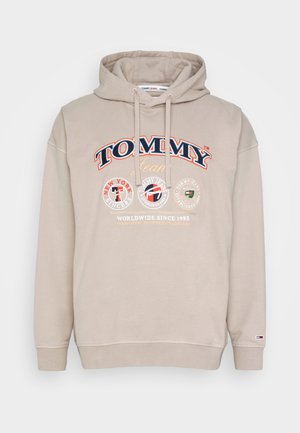 Sweat à capuche beige avec cordon de serrage, arborant un grand logo "TOMMY Jeans" en rouge et bleu, avec des accents graphiques circulaires à l'avant.
