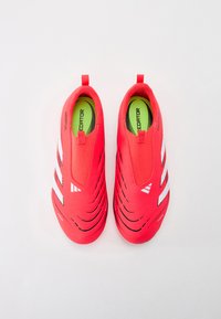Baskets de sport rouge vif avec des rayures blanches, design sans lacets, tige texturée et semelle intérieure verte marquée "PREDATOR."