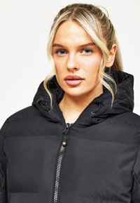 Melnā pūkaini jaka ar kapuci, ar quilted struktūru, rāvējslēdzēja aizdari un stieplem. Gluda auduma virsma ar minimālu apdari.