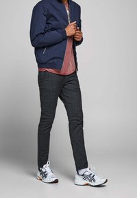 Navy bomber jacket, jasnoczerwony t-shirt, szare spodnie w wzór i białe buty sportowe z czarnymi akcentami. Dopasowany krój, casualowy wygląd.