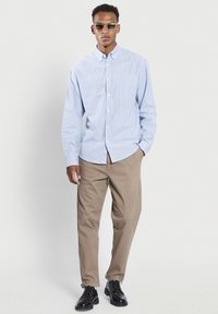 Blauw en wit gestreepte button-up shirt, relaxed fit, met beige broeken en zwarte schoenen. Accessoires omvatten rechthoekige zonnebrillen.