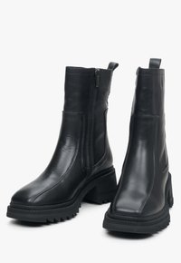 Zwarte enkellaarzen van glad leer, met een zijrits, een chunky hak en een rubberen zool met een zigzagpatroon.