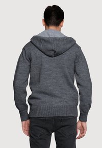 Szara dzianinowa bluza z kapturem w średnim odcieniu szarości, z prążkowanymi mankietami i dołem. Charakteryzuje się teksturowanym wykończeniem i luźnym krojem, odpowiednia do codziennego noszenia.