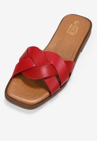 Sandalia deslizante de cuero rojo con un diseño de tira trenzada. La plantilla es color beige, y la suela es marrón, con un estilo plano y punta abierta.