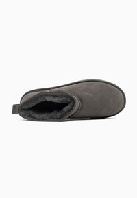 Zapatilla de ante gris con suave forro de piel, con parte trasera cerrada y una lengüeta; punta redondeada y suela plana. Textura lisa con un diseño sencillo.