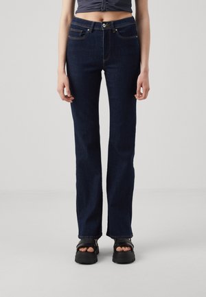 Person wearing dark blue straight-leg jeans, black platform sandals, and a cropped ruched navy top, standing against a plain gray background.