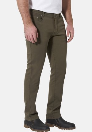 Man wearing olive green slim-fit pants and black ankle boots, standing against a plain light background.