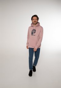 Felpa rosa chiaro con un logo blu navy che recita "PROTEST" sul davanti, dotata di cappuccio con cordini, polsini a costine e tasca a canguro.