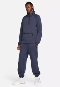 Pile blu navy con collo alto e zip, dotato di tasca frontale, abbinato a pantaloni jogger blu navy con tasche laterali e polsini elasticizzati.