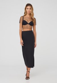 Top in rete nera con maniche corte sopra una gonna nera aderente con uno spacco laterale. L'outfit presenta un effetto elegante e fluido, con un design minimale.