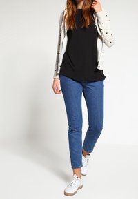 Cárdigan gris claro con lunares negros sobre una camiseta negra, combinado con vaqueros azules y zapatillas blancas con suelas beige.