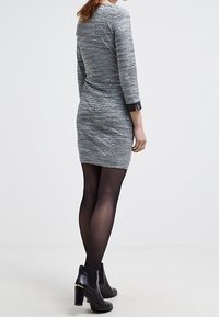 Šedé texturované šaty s dlouhými rukávy a výstřihem do lodičky, kombinované s černými kotníkovými botami, nošeny přes průhledné černé punčochy.