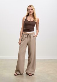 Bruine tanktop, beige wijde broek met elastische tailleband en zijzak, gladde textuur, gedragen met bruin sandaal. Eenvoudig, casual ontwerp.