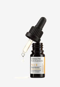 Sort glassflaske med hvit og oransje etikett, pipettehette som doserer en lys gul serum, med fet tekst og små grafiske elementer.