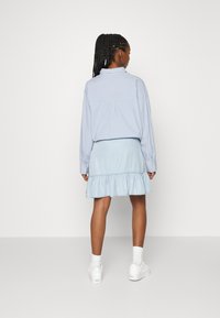 Camisa azul-clara de botão com mangas longas, combinada com uma saia de ganga azul-clara com bainha assimétrica. Ténis brancos completam o visual.