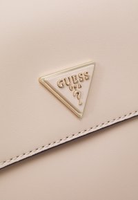 Borsa in pelle sintetica rosa chiaro con una placca logo triangolare dorata e dettagli di cucitura sottili lungo il bordo superiore.