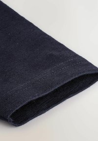 Tissu en coton marine, avec une texture lisse et un ourlet cousu au niveau du poignet. Design simple, vue en gros plan de l'ouverture de la manche.