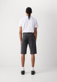 Svarta denimshorts med en lös passform, som har två bakfickor och en kontrasterande gul etikett, tillsammans med en vanlig vit t-shirt.