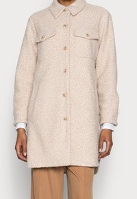 Giacca in pile beige oversize con collo, due tasche sul petto e chiusura con bottoni, caratterizzata da una finitura testurizzata.