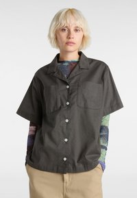 Chemise à manches courtes, gris foncé, avec un col, deux poches poitrine, des boutons blancs et un tissu texturé.