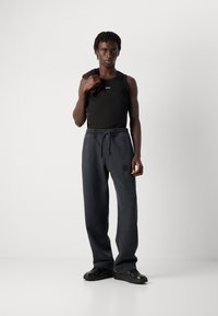 Black tank top with red logo, paired with dark gray, loose-fitting pants with an elastic waistband. Black shoes complete the outfit.