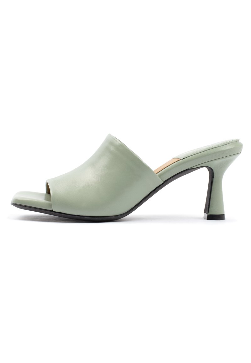 Mule aperti in pelle verde con design curvo, tacco affusolato e texture liscia. La suola presenta un accentuazione nera per contrasto.