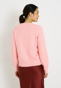 Suéter rosa suave con un ajuste relajado, puños y dobladillo acanalados, con una textura peluda. Combinado con una falda fluida color burdeos.