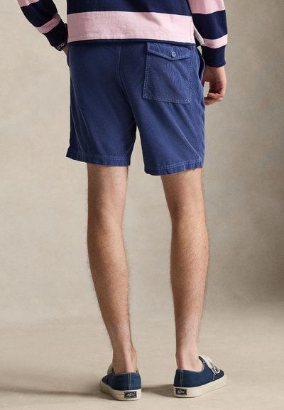 Μακριά μπλε σορτς κατασκευασμένα από βαμβάκι με υφασμένη υφή, διαθέτουν πίσω τσέπη με κλείσιμο με κουμπί και γύρισμα στο τελείωμα.