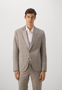 Costume gris clair avec veste et pantalon sur mesure, doté de revers en pointe, de deux boutons et d'une chemise blanche. Design simple, texture lisse.