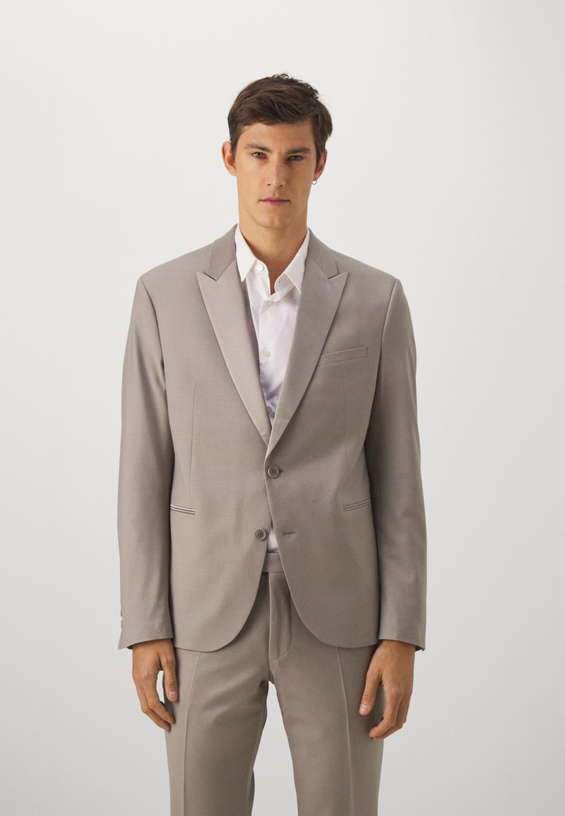 Costume gris clair avec veste et pantalon sur mesure, doté de revers en pointe, de deux boutons et d'une chemise blanche. Design simple, texture lisse.