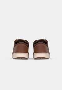 Zapatos de cuero marrón con un diseño redondeado, suelas de color crema y cuellos acolchados, con un mínimo de marca en el talón.