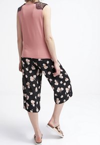 Różowa bezrękawnikowa bluzka z czarnymi koronkowymi akcentami na ramionach, w połączeniu z czarnymi kulotami w kwiatowy wzór, wykonanymi z miękkiego materiału i charakteryzującymi się luźnym krojem.