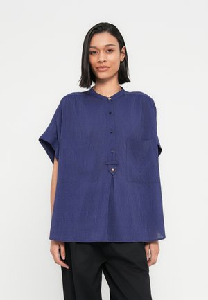 Camisa de manga corta azul marino con cuello mandarín, botones frontales, textura plisada y dos bolsillos delanteros. Corte holgado.