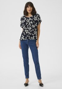 Blusa floreale blu marino con fiori bianchi, tessuto morbido, maniche corte, abbinata a jeans blu e ballerine nere. Design semplice e in forma rilassata.