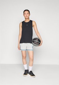 Sort ærmeløs skjorte med et logo, lysegrå shorts med blå accenter, hvide sokker og sorte basketballsko, holder en sort basketball.