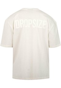 Cremefarbendes Baumwoll-T-Shirt mit lockerer Passform. Auf der Rückseite befindet sich große, strukturierte "DROPSIZE"-Schrift. Kurze Ärmel und runder Halsausschnitt.