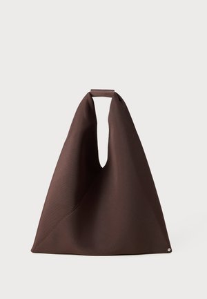 Brown fabric tote bag with a unique shape, featuring a wide opening, textured surface, and a small circular accent at the base.