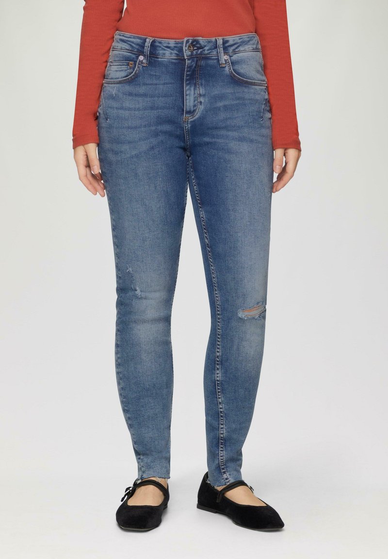 Jean en denim extensible bleu avec une coupe skinny, présentant une taille haute, des détails déchirés au niveau des genoux et un design classique à cinq poches.