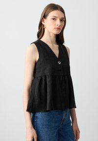 Top senza maniche nero con scollatura a V, caratterizzato da un orlo peplum arricciato e un dettaglio con bottone argentato sul davanti. Finitura in tessuto testurizzato.