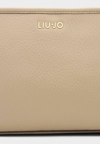 Beige leren portemonnee met een gestructureerd oppervlak, voorzien van een gouden "LIU•JO" logo aan de bovenkant en gestikte randen voor duurzaamheid.