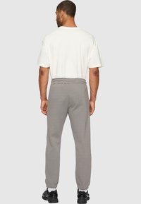 Grå joggebukser med elastisk midje og smalere mansjetter, sammen med en løspasset hvit t-skjorte. Teksturert stoff, uformelt design.